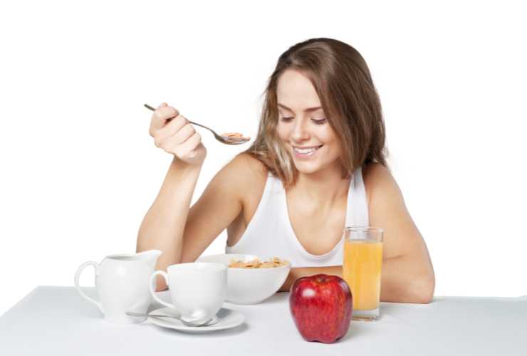donna che fa colazione con cereali, succo e mela