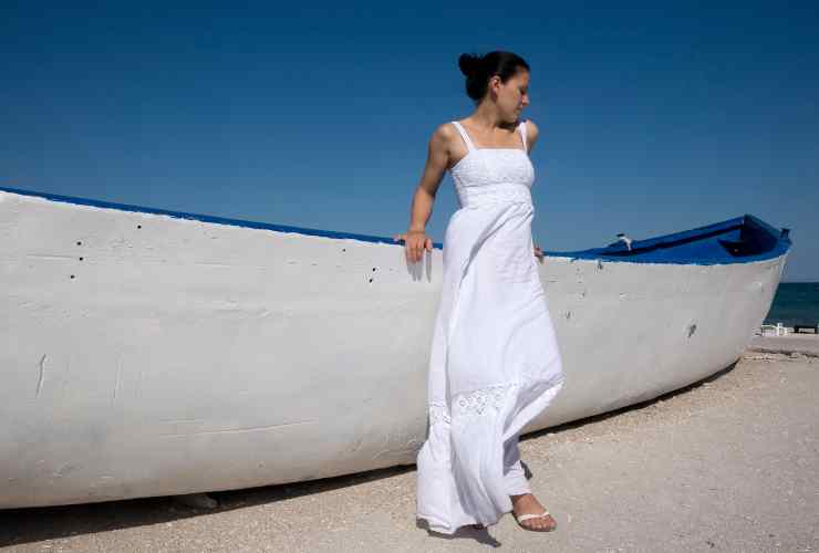 Ragazza con vestito bianco al mare vicino ad una barca