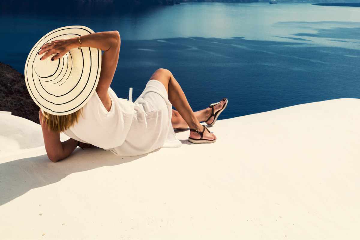 donna con abiti bianchi e cappello sdraiata su terrazza vista mare