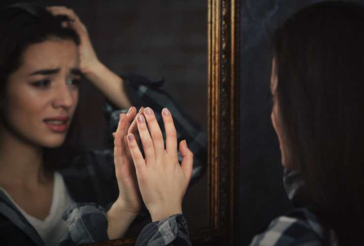 donna triste che guarda il suo riflesso nello specchio